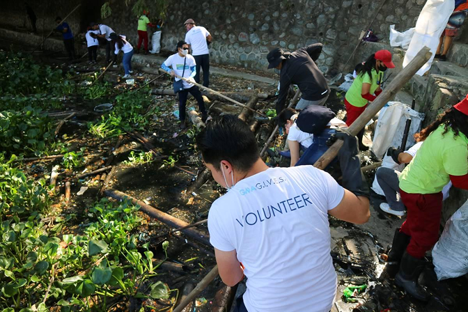 A Revolve volunteer pulling plastic waste out of a silted-up waterway alongside a clean-up crew